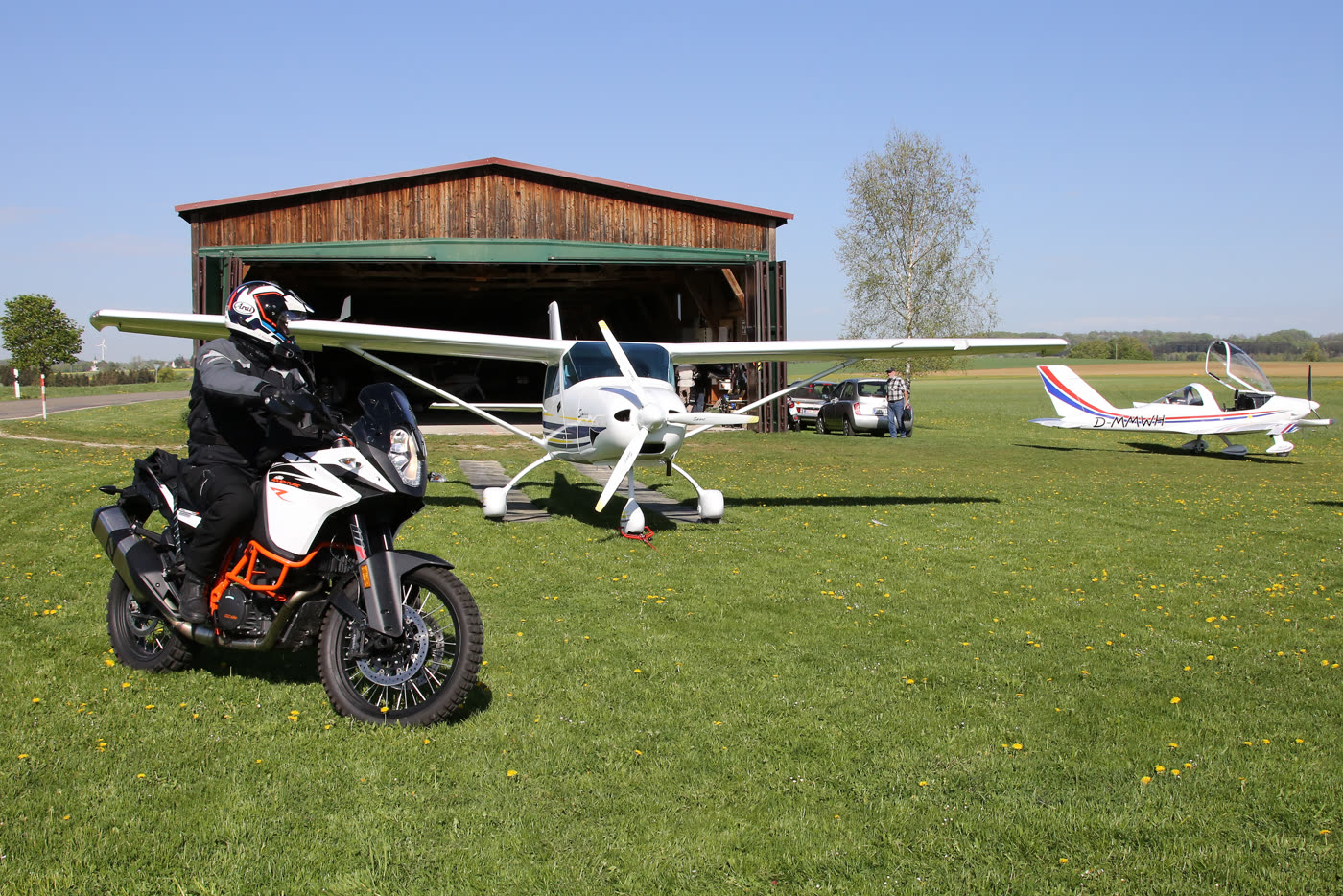 Motorrad vor abgestellten Segelflugzeugen auf dem ehemaligen Feldflugplatz